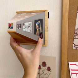 Hand holding a wooden display showcasing art pieces against a wall, perfect for modern decor and creative spaces.